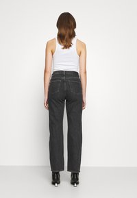 Pantalones de mezclilla negros de pierna ancha con una cintura alta y dos bolsillos traseros, combinados con una camiseta sin mangas blanca y botas de tobillo negras de tacón.