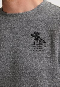 Grijze sweatshirt gemaakt van zachte stof, met een zwart geborduurd logo van een boom en bergen, ronde hals en ribgebreide manchetten.
