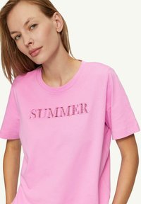 Helles rosa Baumwoll-T-Shirt mit kurzen Ärmeln, das einen bestickten Schriftzug "SUMMER" in einem kontrastierenden Stil über der Brust zeigt.