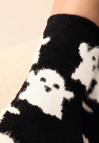 Zwart-witte, pluizige sokken met een spookpatroon, een zachte textuur en een gezellig ontwerp. De sok eindigt bij de enkel.