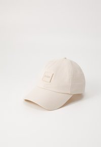 Beeži puuvillane pesapalli müts, millel on ümar kroon, kõver visor ja ruudukujuline logo märk "BOSS" ees.