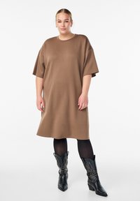 Brun oversized t-shirt kjole, rund halsudskæring, korte ærmer. Båret med sorte læder cowboy støvler med nitter.