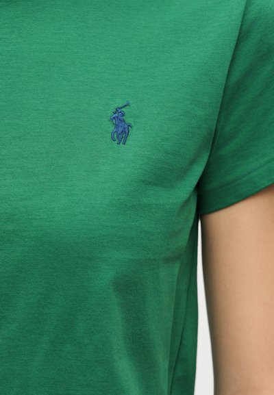 Πράσινο πουκάμισο που φοριέται από ένα άτομο, με ένα μικρό μπλε κεντημένο λογότυπο παίκτη πόλο πάνω σε άλογο στο στήθος.