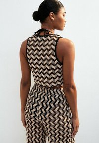 Crop top tricoté brun et crème avec un motif en zigzag, doté d'une fermeture à nouer noire dans le dos, associé à un pantalon taille haute assorti.