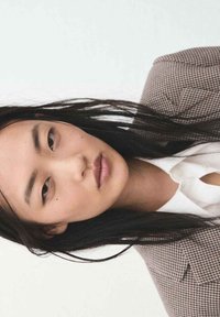 Model met lang donker haar, gekleed in een geruite blazer over een wit shirt. De blazer heeft een gestructureerd ontwerp en klassieke revers.