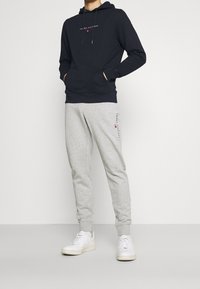 Sudadera de marinero con bolsillo frontal y logo; pantalones de chándal grises con franjas laterales; zapatillas blancas. Conjunto casual y cómodo.
