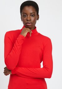 Rotes langärmliges Rollkragenoberteil aus weichem, elastischem Material; mit figurbetontem Schnitt und hohem Kragen.