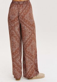 Široké nohavice vyrobené z ľahkého hnedého materiálu s bielym paisley vzorom, s elastickým pásom a bočnými vreckami.