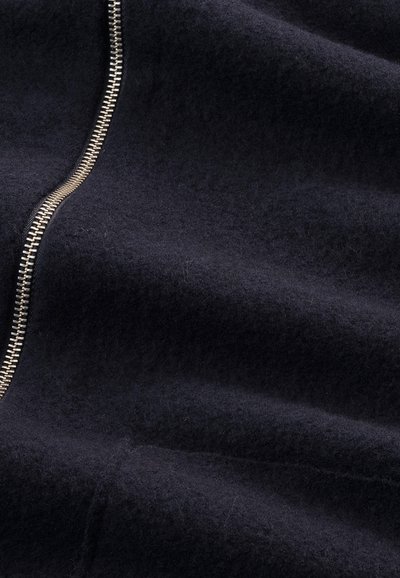 Donker marineblauwe wollen stof heeft een prominente metalen rits langs één kant, wat een textuurscontrast creëert over het gladde oppervlak.