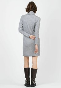 Graues, geripptes Kleid mit langen Ärmeln und hohem Kragen. Getragen mit schwarzen, knielangen Lederstiefeln mit Schnallen.