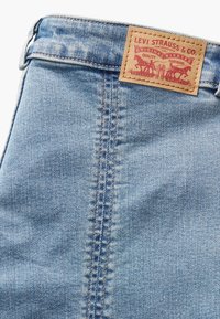 Gros plan d'un jean en denim bleu clair avec une couture verticale visible et un patch en cuir marron de la marque Levi Strauss & Co. près de la taille.
