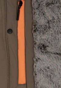 Giacca marrone con pannello in pelliccia sintetica grigia, accento con cerniera arancione e bottone a pressione nero sul lato. Tessuto strutturato che crea contrasto.