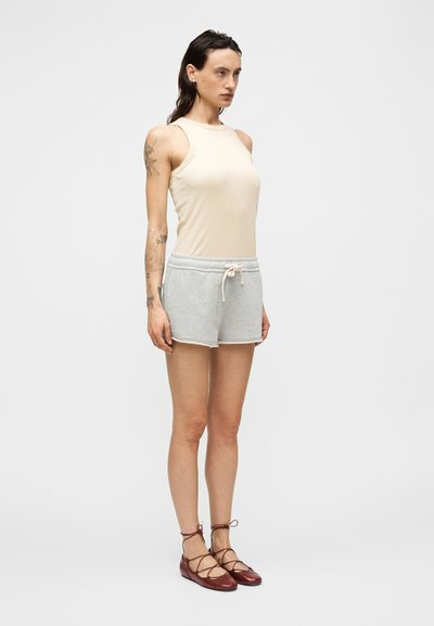 Μπεζ αμάνικη μπλούζα, γκρι σορτς με ελαστική μέση και κορδόνι, κόκκινα μπαλαρίνια με δαντελένιες λεπτομέρειες. Λείο ύφασμα, άνετη εφαρμογή.