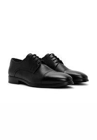 Chaussures habillées en cuir noir avec une finition texturée, bout arrondi et un design classique à lacets. Accents lisses au niveau du bout et du talon.