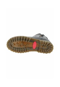 Semelle de botte noire avec un motif de crampons prononcé et un logo ovale rouge au centre, vue par le dessous sur un fond blanc.