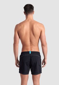 Pantaloni da bagno neri con vita regolabile, caratterizzati da dettagli di cucitura bianchi e un'etichetta blu sul retro.
