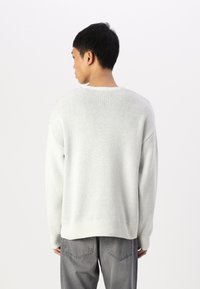 Lichtgrijze gebreide trui met een ronde halslijn en geribde mouwen en onderkant. Losse pasvorm, met een gestructureerde stof, gedragen over grijze jeans.