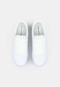 Baskets Lacoste blanches avec une tige en cuir lisse, logo jaune contrastant et six œillets pour lacets blancs. Intérieur rembourré pour plus de confort.