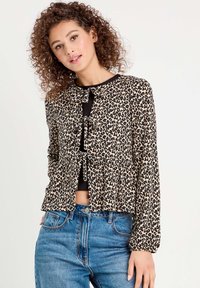 Blouse en imprimé léopard avec manches longues, fermeture à nouer à l'avant et ourlet en style peplum, fabriquée en tissu léger. Portée avec un jean taille haute.