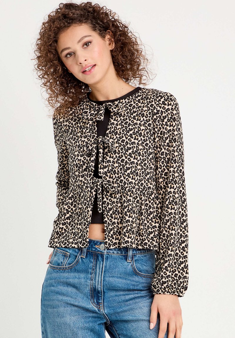 Blouse en imprimé léopard avec manches longues, fermeture à nouer à l'avant et ourlet en style peplum, fabriquée en tissu léger. Portée avec un jean taille haute.