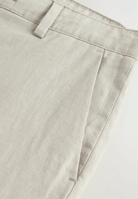 Pantaloni in lino beige chiaro con una finitura testurizzata, dotati di frontale piatto, tasche laterali e un design della vita pulito.