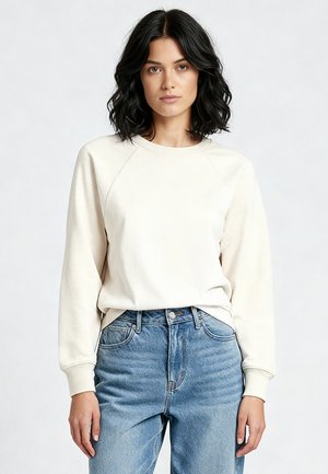 Crèmekleurige sweatshirt met raglanmouwen, zachte textuur en geribbelde manchetten, gecombineerd met een spijkerbroek met hoge taille. Eenvoudig ontwerp.