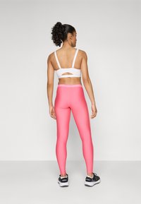 Rosa leggings med en jevn tekstur og et merkevarebelte, kombinert med en hvit sports-bh med utskjæring og justerbare stropper.