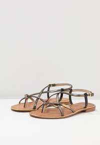 Sandales plates avec des lanières dorées métalliques et noires, présentant un motif texturé sur les lanières et une semelle intérieure en cuir lisse.