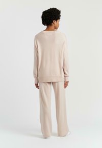 Pull en maille rose clair avec une coupe décontractée et des manches longues, associé à un pantalon large assorti. Texture douce et design minimaliste.