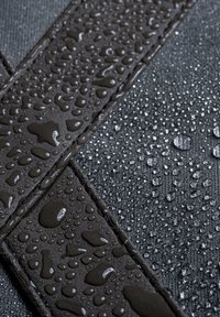 Tessuto nero testurizzato con gocce d'acqua, che mostra una combinazione di superfici lisce e ruvide, evidenziando una caratteristica impermeabile.