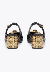 Black patent leather sandals with a rounded toe, ankle strap, and a gold block heel adorned with circular studs.