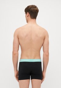 Schwarze Boxershorts mit einem hellblauen Bund, der mit "Calvin Klein"-Branding versehen ist. Glattes Material mit einer taillierten Passform.