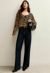Leopardprint cropped trui gemaakt van zacht materiaal, gecombineerd met high-waisted, wijde donkerblauwe spijkerbroek en glanzende zwarte enkellaarzen.