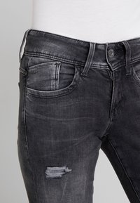 Czarne dżinsy o slim fit, z lekkimi przetarciami i klasycznym pięciPocketowym wzorem. Materiał ma subtelną teksturę.