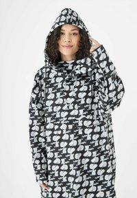 Schwarzer Regenmantel mit Kapuze, der ein weißes Cartoon-Muster aufweist. Das Material wirkt glatt und wasserdicht, hat eine entspannte Passform und Kordelzug-Akzente.