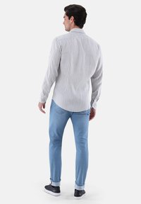 Gestreiftes langärmeliges Hemd in Hellgrau und Weiß, mit Button-Down-Kragen, dazu schlanke hellblaue Jeans und dunkle Sneakers.