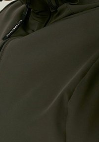 Tmavě zelená měkká bunda s vysokým límcem, přičemž má přední zip a nastavitelné šňůrky. Hladká textura s minimálními detaily.