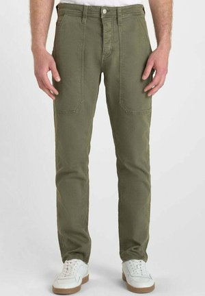 Pantalones de algodón verde oliva con corte recto, que presentan bolsillos delanteros y costuras reforzadas, combinados con zapatillas blancas.