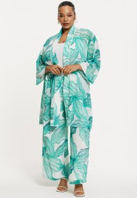 Kimono-stijl jurk van doorzichtig materiaal, met een groen loofpatroon op een witte achtergrond, brede mouwen en een bijpassende strikceintuur.