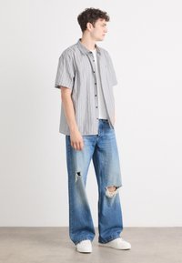 Kortermet stripet skjorte i grått og hvitt, kombinert med lyseblå, slitte viddejeans og hvite joggesko. Uformell, avslappet passform.