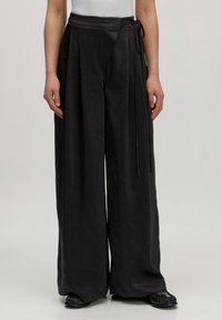 Zwarte wijde broek van gladde stof, met een wikkeldesign en strikjes bij de taille en subtiele plooien aan de voorkant.
