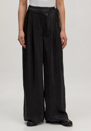 Zwarte wijde broek van gladde stof, met een wikkeldesign en strikjes bij de taille en subtiele plooien aan de voorkant.