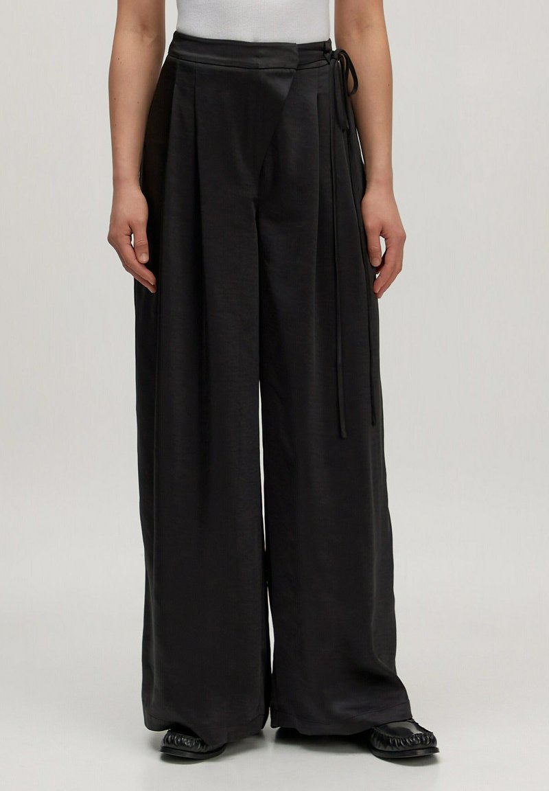 Zwarte wijde broek van gladde stof, met een wikkeldesign en strikjes bij de taille en subtiele plooien aan de voorkant.