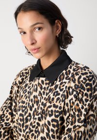 Majica s leopard printom uz crni ovratnik i detaljima s gumbima, izrađena od mekog, teksturiranog materijala s bogatim rukavima.