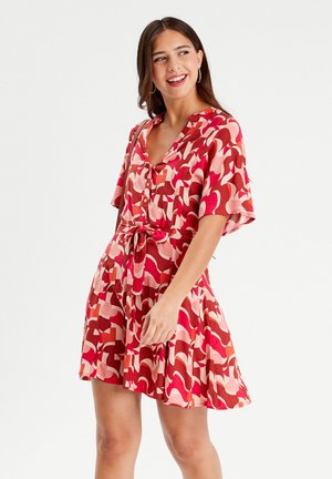 Short dress with a v-neck, short sleeves, and a drawstring waist. Made from a smooth, colorful fabric featuring abstract red and pink patterns.