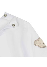 Wit babyshirt met drukknoopsluiting en textuur 'schaap' borduursel accent op de linker mouw. Zachte stof met een gladde afwerking.