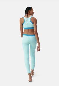 Top sportiv de culoare albastru deschis și colanți asortati, cu o textură netedă și accente contrastante de culoare albastru închis, văzuți din spate.