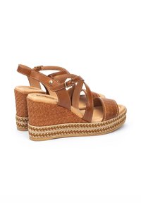 Sandalias de cuña marrones con diseño de tiras cruzadas, cuero texturizado y suela de rafia trenzada con detalles trenzados. Cierre ajustable con hebilla.