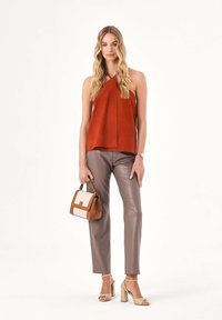 Rdzawy top bez rękawów, beżowe spodnie z imitacji skóry, beżowe sandały na słupku oraz mała torebka z brązowo-kremowym wzorem.