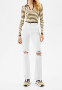White ripped jeans with a straight-leg fit, paired with a brown and yellow zigzag-patterned top featuring a V-neck and long sleeves.